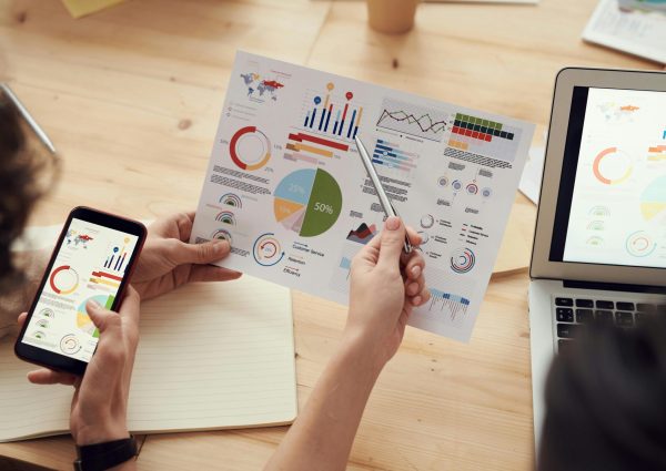Team members analyze charts during a business meeting with laptops and smartphones.